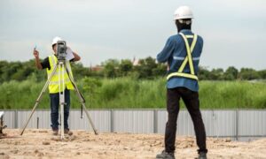 Two land surveyors using a total station on a construction site representing boundary survey delays in real estate