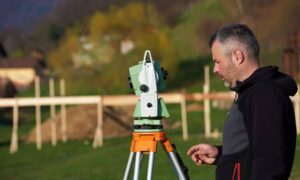 Land surveyor using a total station during an elevation survey to record precise land measurements for documentation