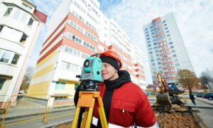 Licensed land surveyor using a total station at an urban construction site to ensure precise building alignment
