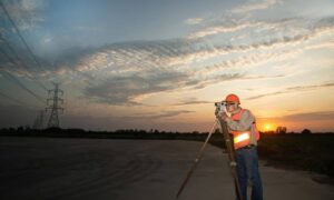 Land surveyor sunset field - ALTA SURVEY Missouri A land surveyor using a tripod and optical equipment at sunset while conducting an ALTA Land Title Survey under a glowing sky