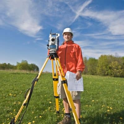 Cadastral surveyor using a total station to verify property boundaries after storm damage