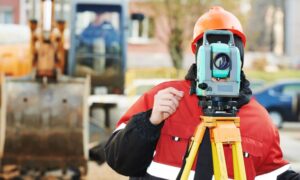 Surveyor performing land surveying with a total station to check property boundaries before repairs