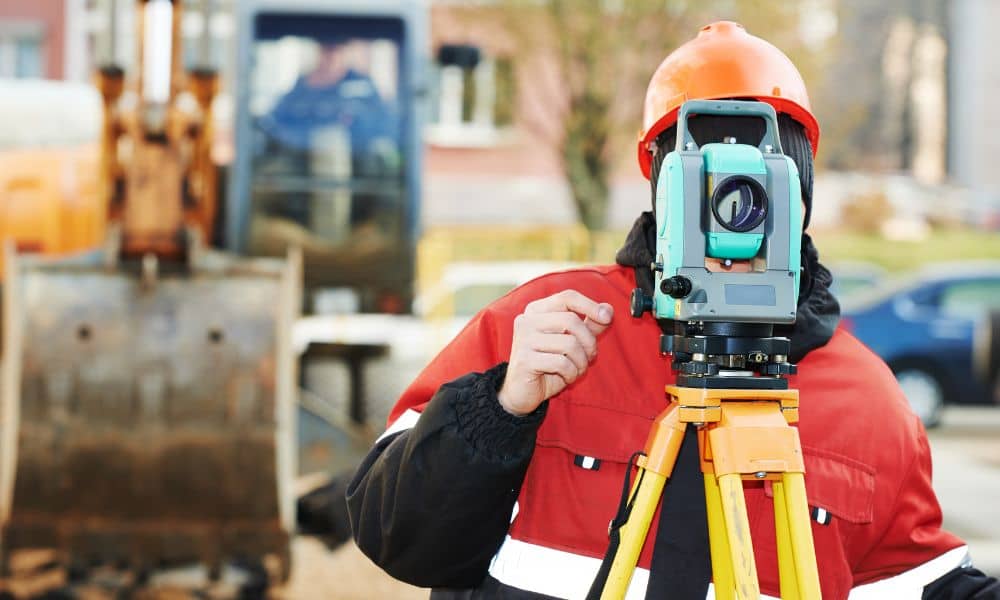 Surveyor performing land surveying with a total station to check property boundaries before repairs