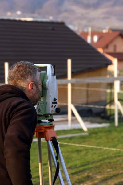 A land surveyor measuring a residential property boundary before confirming the fence line