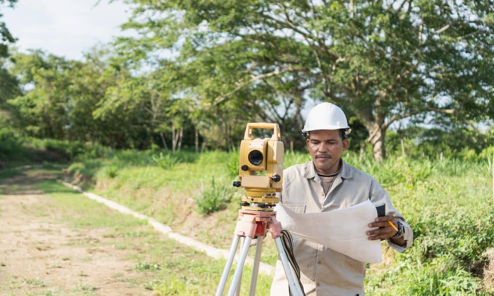 Surveyor reviewing a plat of survey beside a total station at a grassy site